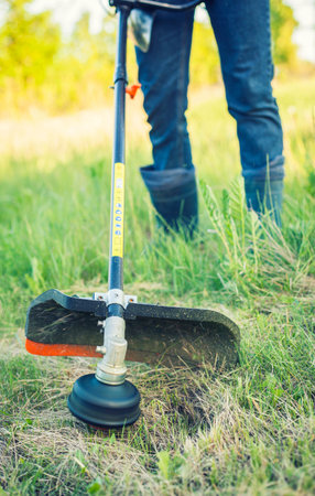 worker mows green grass on the lawn with hand trimmer. lawn care. weed control. Woman with gasoline...