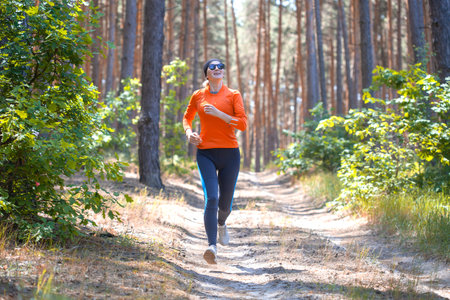 young girl on a morning run in a sunny pine forestの写真素材