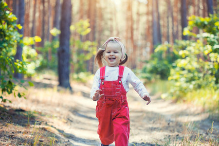 Portrait of smiling three years old caucasian child girl runs on the trail in the pine forest. Waving hands. Forest on bright light background.の写真素材