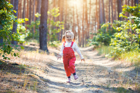 Portrait of smiling three years old caucasian child girl runs on the trail in the pine forest. Waving hands. Forest on bright light background.の写真素材