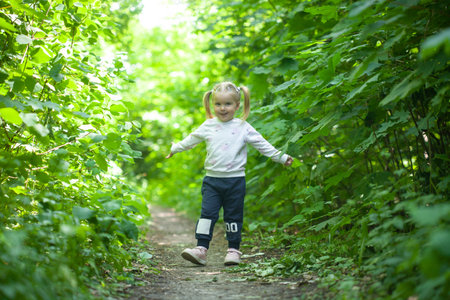 Portrait of smiling girl runs on the trail in the deciduous forest. Waving hands. Forest on bright light background.の写真素材