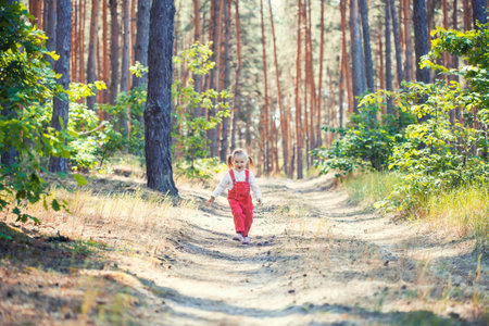 Portrait of smiling three years old caucasian child girl runs on the trail in the pine forest. Waving hands. Forest on bright light background.の写真素材