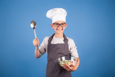 cheerful brunette boy cook in a chefs hat and apron prepares a salad. studio photo. My future...