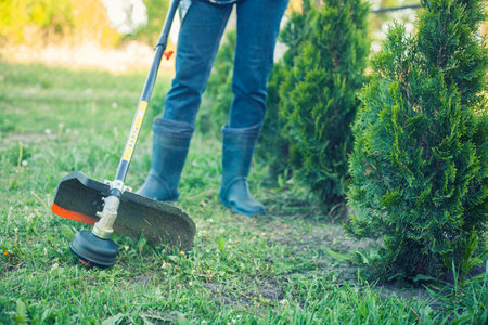 worker mows green grass on the lawn with hand trimmer. lawn care. weed control. Woman with gasoline mower cutting grass. Grass trimmer worker, garden work.の写真素材