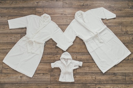 Three white Bathrobe for family on wooden backgroundの写真素材