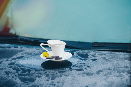 Hot strong Cup of coffee with chocolate on the frozen hood of the blue car. Morning, cold, frost, hoarfrost, waitingの写真素材