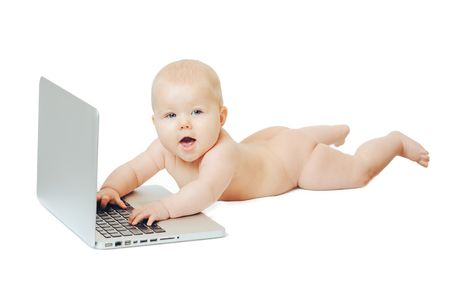 Happy little baby lying naked in front of a silver laptop and presses a button.の写真素材