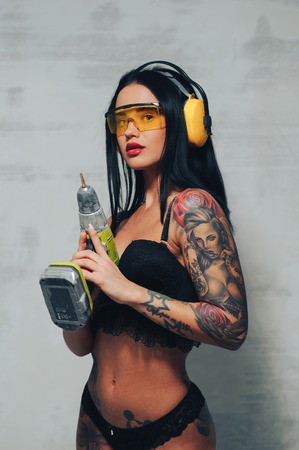 Sexy girl construction Builder in yellow with glasses and headphones holding a drill like a gunの写真素材