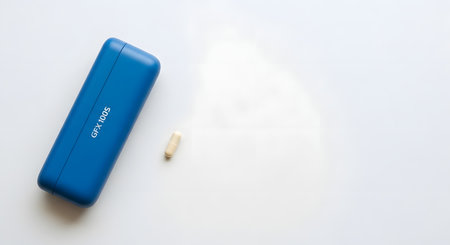 A blue rectangular object, possibly a case or power bank, lies on a plain white surface next to a small, light-colored item.の素材