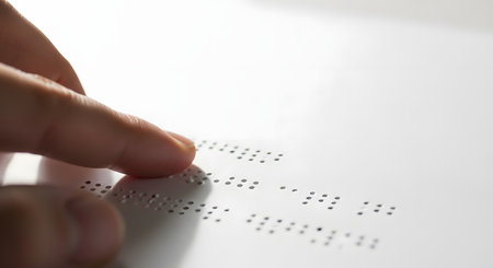 A macro view of a finger feeling the raised dots of a Braille system on a white page. A concept for blindness, learning, tactile communication, and accessibility for the visually impaired.の素材