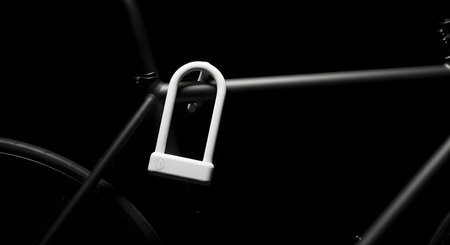 A white U-lock secured to the frame of a bicycle, presented against a stark black background.の素材