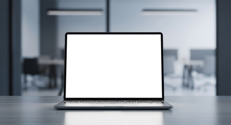 A sleek, modern laptop with a blank white screen sits on a polished desk in a contemporary office setting. The background is blurred, showing office furniture and lighting.の素材