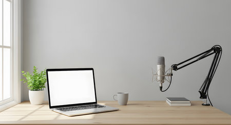 A clean and modern podcast studio setup featuring a laptop, microphone on an arm, a plant, and a book on a wooden desk.の素材