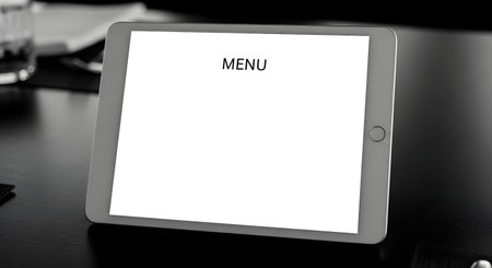 A close-up, black and white shot of a tablet device with a blank white screen showing the word MENU, placed on a dark, textured surface.の素材
