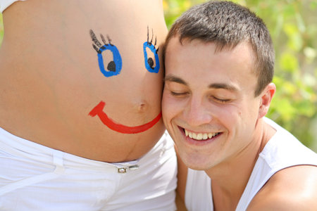 Painted happy smiley face on the belly of pregnant womanの写真素材