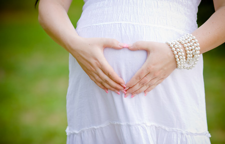 Woman holding her hands in a heart shape on her pregnant bellyの写真素材