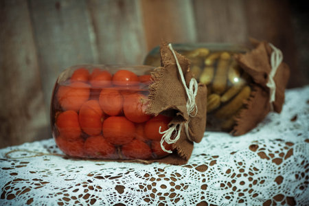 Canned cucumbers and tomatoes in two glass banks on a wooden backgroundの写真素材
