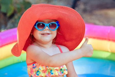 The beautiful little girl in a bathing suit and a hat swims in the pool