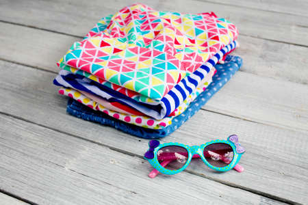 Kidswear pile and sunglasses on a white wooden background. Stack of colorful cotton children clothing on wooden background.の写真素材