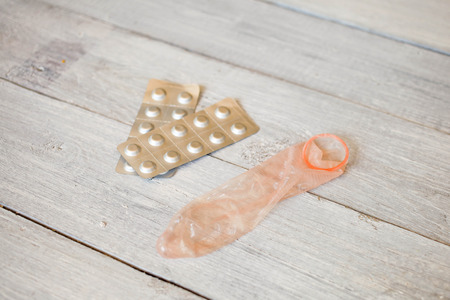 The used condom and tablets on a white wooden backgroundの写真素材