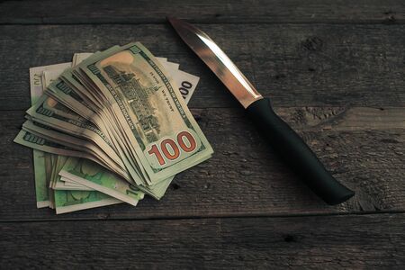 A knife and some fanned out cash laying on wooden background . This works for all sorts of illegal activities such as prostitution, drug dealing, and gang activity.の写真素材