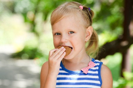 A little happy girl eats an avenaceous thin captain on nature.の写真素材