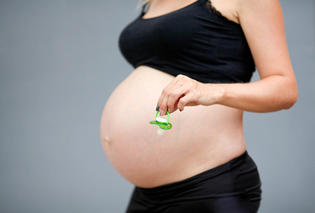 The pregnant woman's stomach on a gray background. The hand of the pregnant woman holds a pacifier in hand.の写真素材