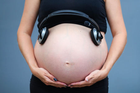 Pregnant woman's belly. Unborn child listens to music with headphones.の写真素材