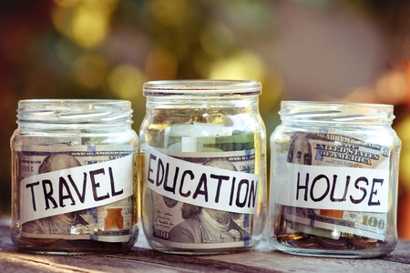 A lot coins in glass money jar on the wood table. Saving for house, travel and educatiuonの写真素材