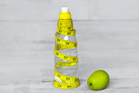 Bottled water for healthy life over yellow measuring tape and green apple. Symbol of health and dietの写真素材