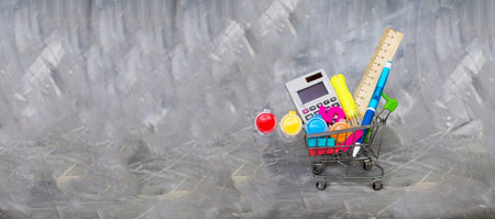 Shopping cart for school supplies on a gray background.