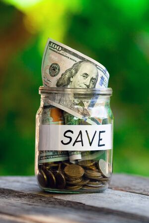 The hundred-dollar note looks out of a glass jar on an indistinct green background. Word save paper label.の写真素材