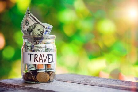 Glass jar with dollars and the word travel paper label. Travel budget concept. Travel money savings in a glass jar , copy space .の写真素材