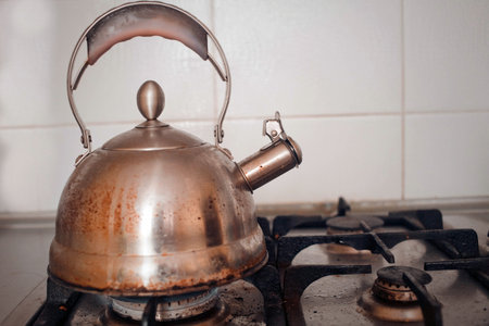 The dirty metal teapot is installed on the gas stove, a side view.