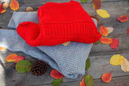 Folded knitted things, autumn leaves on a wooden background.