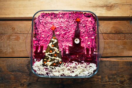 Home New Year is herring salad under a coat with the decoration of the Russian Kremlin and a tree on a wooden background. Russian cuisine.の写真素材