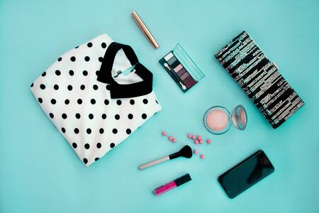 Women is dress print polka dots, bag, cosmetics, lipstick, eye shadow, powder, blush , mascara and smartphone on a blue background.の写真素材