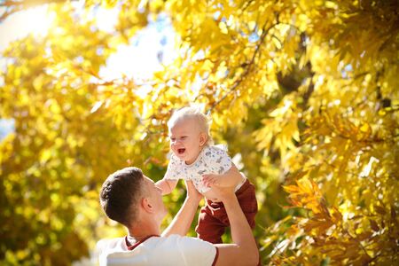 Happy father throws his adorable baby up in autumn park. Father and son spend a day together.の写真素材