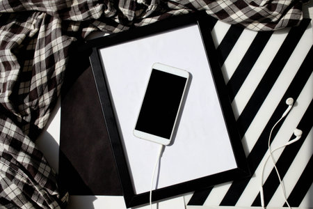 A white smartphone and headphones on a black white background with a strip. Top view, shadows