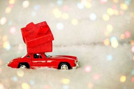 Krasnodar, Russia - December 10, 2019: Red retro toy car delivering  present of red box on white background , bokeh . February 14 card, Valentine's day , New year. Copy space.のeditorial素材