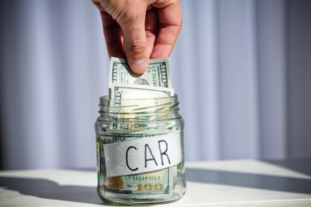 Male hand puts 100 dollars in a glass jar with the text car. Concept of saving money.