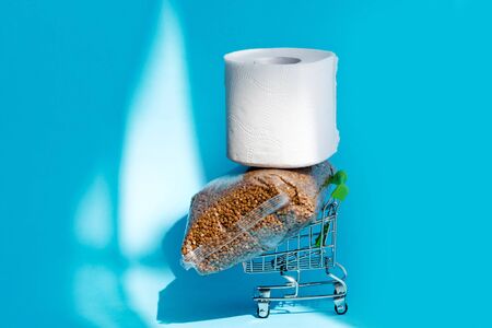 Buckwheat and toilet paper on a shopping cart  on blue background. Consumer buying panic about coronavirus covid-19 concept. Stocking up essentials for home quarantineの写真素材