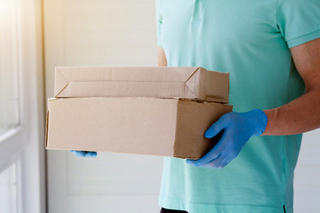 Male hands in blue rubber gloves hold a cardboard box.  Fast and free Delivery transport. Online shopping and Express delivery. Quarantineの写真素材