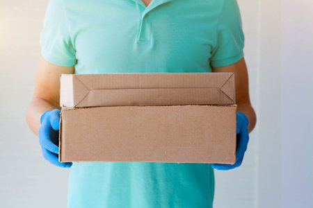 Ð¡ourier man delivers the package to the door, contact less delivery. Male hands in blue rubber...