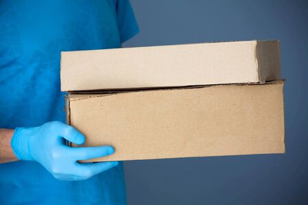 Ð¡ourier man delivers the package to the door, contact less delivery. Male hands in blue rubber gloves hold a cardboard box. Home delivery, online order.  Online shopping .の写真素材