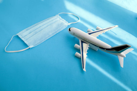 Plane model and face medical mask on a blue background . Flight cancellation due to the impact of coronavirus (COVID-19) concept. Top viewの写真素材
