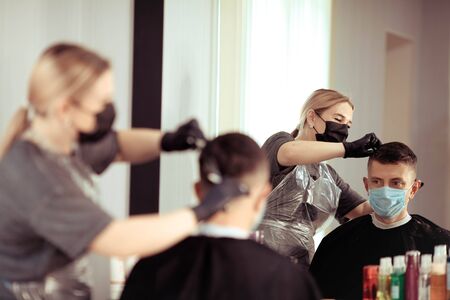 A hairdresser with security measures for Covid-19, cuts hair with a scissors to a man in a medicine mask, social distance, cutting hair with a medical mask and rubber glovesの写真素材