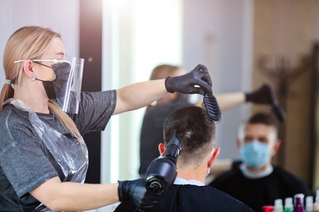 A hairdresser with security measures for Covid-19, blow-dry a man in a medicine mask, social distance, cutting hair with a medical mask, eye mask and rubber gloves in a beauty salonの写真素材