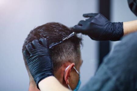 A hairdresser with security measures for Covid-19, holds scissors in his hands and cuts a man, social distance, cutting hair with rubber gloves in a beauty salonの写真素材