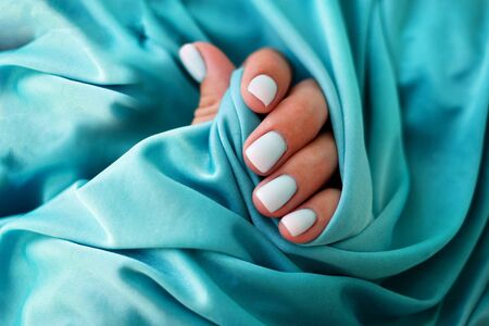 Female hands with a beautiful manicure on a blue background. Summer trend, blue gradient on the nails with gel polish, shellac. Short nailsの写真素材
